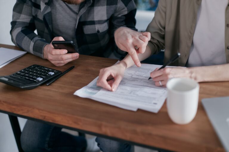 Couple de plus de 50 ans analysant ses charges fixes avec des contrats, un carnet de budget et une calculatrice